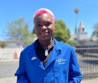 smiling black teen wearing a blue lab coat that reads UCSF Benioff Children's Hospital Oakland CHAMPS