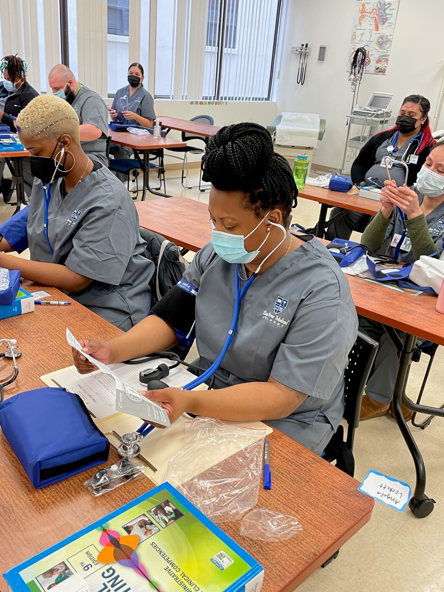 Adult students in classroom wear stethoscopes and masks learning about the healthcare field